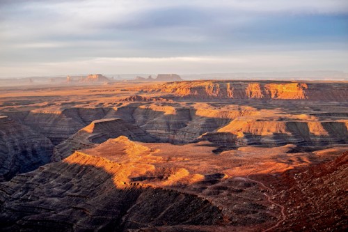 A vast desert landscape with layered rock formations, bathed in warm sunlight under a clear sky.