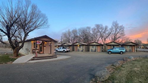 A small motel with several cabins, a welcoming office, and trees against a colorful sunset sky.