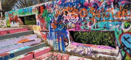 Colorful graffiti covers a concrete wall and steps, featuring various designs and vibrant hues in an outdoor setting.