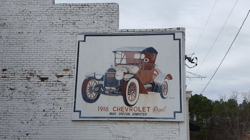 Mural of a 1916 Chevrolet Royal mail roadster on a white brick wall.