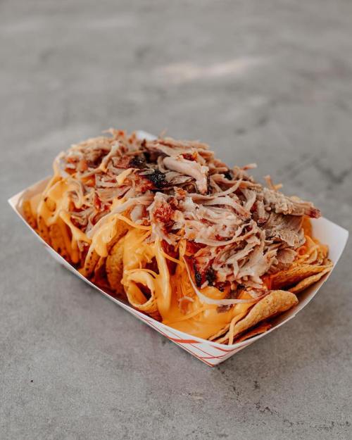 A tray of nachos topped with melted cheese and shredded meat, served on a gray surface.