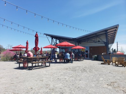 Outdoor dining area with red umbrellas, picnic tables, and a modern building under a clear blue sky.