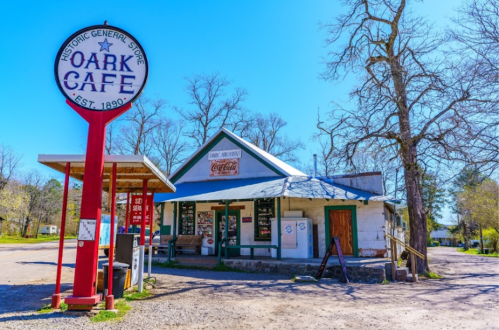 Historic Oark Cafe, established in 1890, features a vintage sign and a charming exterior surrounded by trees.