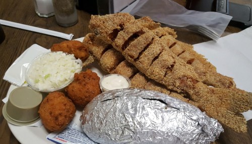 A plate of fried fish fillets, hushpuppies, coleslaw, and a baked potato wrapped in foil.