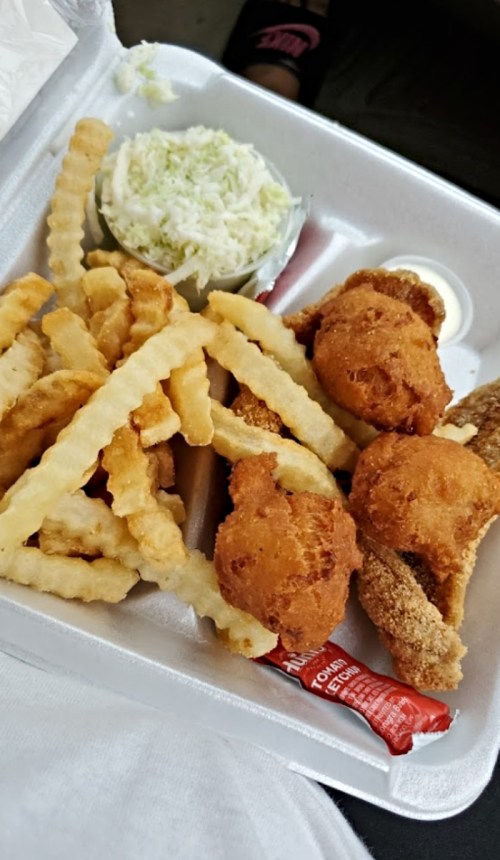 A takeout container with fried chicken, crinkle-cut fries, coleslaw, and a packet of sauce.