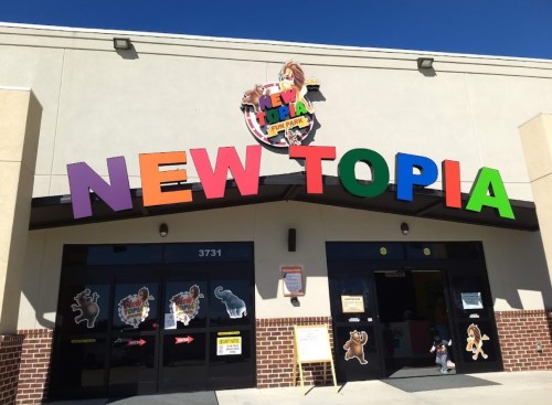 Colorful sign reading "NEW TOPIA" on a fun park building entrance with playful animal decorations.