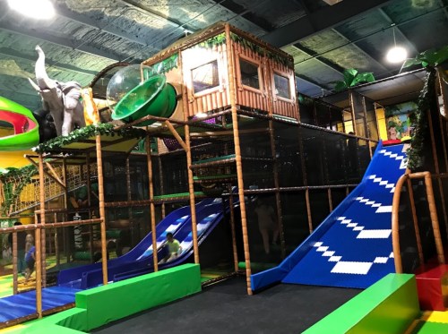 A colorful indoor play structure with slides, climbing areas, and jungle-themed decorations.
