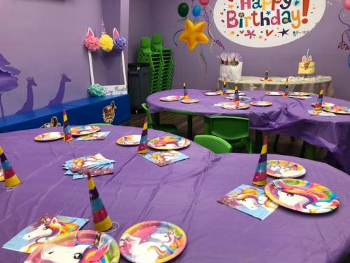 A colorful birthday party setup with purple tables, unicorn-themed decorations, and party hats.