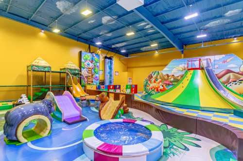 Colorful indoor playground featuring slides, climbing structures, and a ball pit in a bright, cheerful environment.