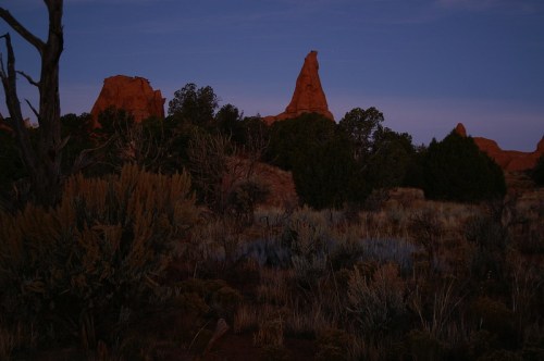 Silhouetted rock formations at dusk, surrounded by sparse vegetation and a twilight sky.