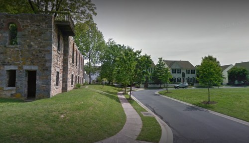 A quiet neighborhood street with a mix of modern homes and a stone building, surrounded by greenery.