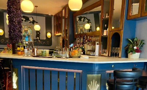 A stylish bar with a marble countertop, colorful decor, and a variety of drinks displayed on shelves.