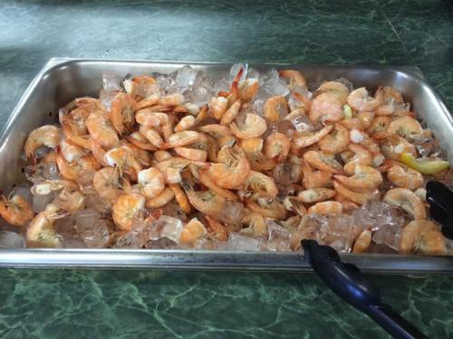 A tray filled with cooked shrimp on ice, garnished with lemon slices and served with tongs.