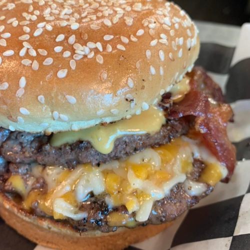 Close-up of a juicy burger with sesame seed bun, melted cheese, bacon, and layers of beef patty.
