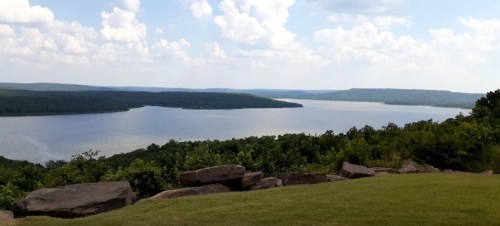 A scenic view of a calm lake surrounded by green hills and a blue sky with fluffy clouds.