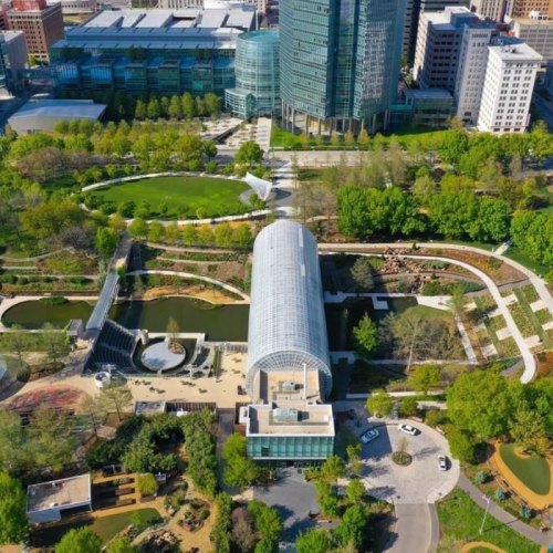 Aerial view of a modern park with greenery, water features, and buildings in an urban setting.
