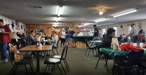A busy dining area with people eating and socializing at tables, featuring a casual, community atmosphere.