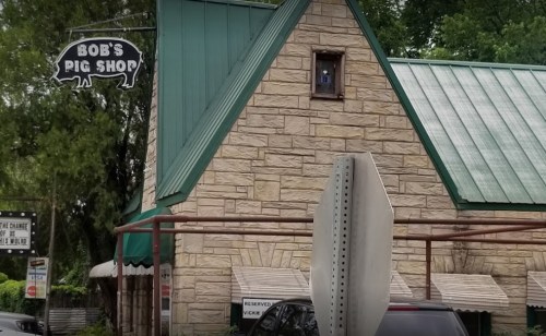 A stone building with a green roof and a sign reading "Bob's Pig Shop," featuring a parking sign in front.