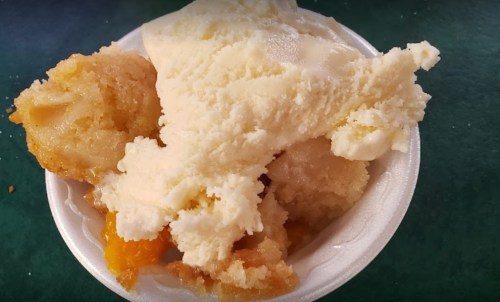 A bowl of creamy vanilla ice cream with chunks of peach and a crumbly topping.
