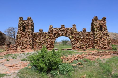 Stone ruins of a castle-like structure with two towers and an archway, set against a clear blue sky.