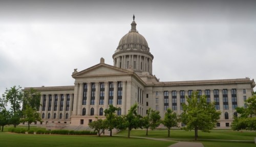 Historic building with a large dome, surrounded by green trees and a cloudy sky.