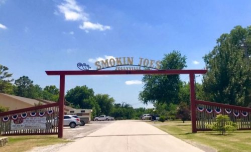 Entrance sign for Smokin Joe's in a sunny outdoor setting, decorated with red, white, and blue bunting.