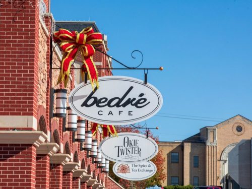 Signage for Bedré Café and Okie Twister, decorated with a large red bow, against a clear blue sky.