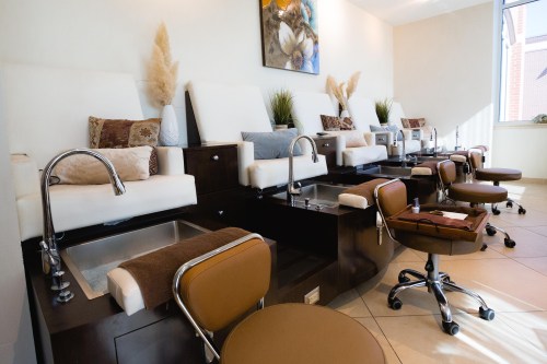 A modern nail salon with comfortable pedicure chairs and sinks, decorated with plants and artwork on the wall.