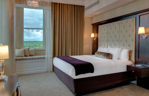 Luxurious hotel room featuring a king bed, elegant decor, and a large window with a scenic view.