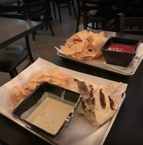 A plate with tortilla chips, a bowl of salsa, and a grilled wrap on a table in a dimly lit restaurant.