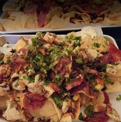 A close-up of a tray of nachos topped with chicken, bacon, cilantro, and various toppings on crispy tortilla chips.