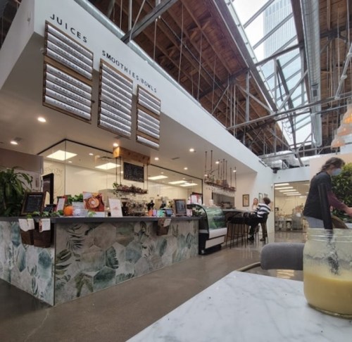 A modern café interior with a juice and smoothie bar, featuring a green-themed counter and customers enjoying their drinks.