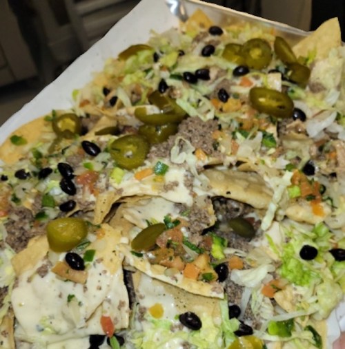 A large plate of nachos topped with ground beef, cheese, black beans, lettuce, tomatoes, and jalapeños.
