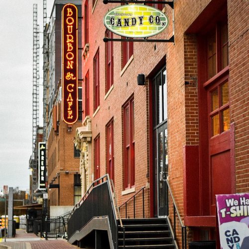A street view of brick buildings featuring signs for Bourbon St. Café and a candy shop.