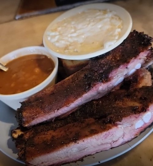 A plate of smoked ribs with sides of baked beans and coleslaw.