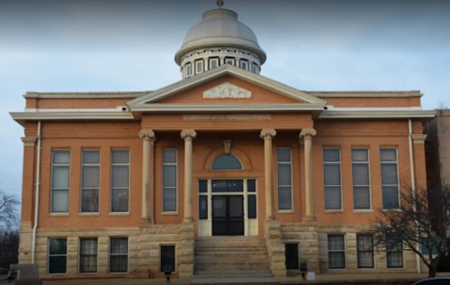 Historic brick building with a dome, featuring large windows and a central entrance, set against a cloudy sky.