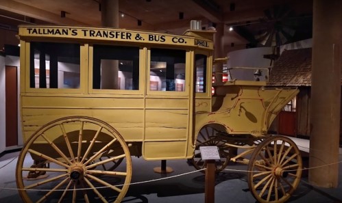 A vintage yellow horse-drawn bus with "Tallman's Transfer & Bus Co." painted on the side, displayed in a museum.