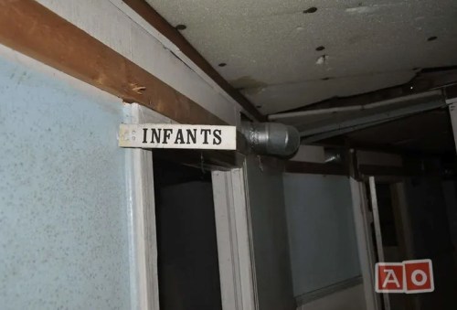 Sign labeled "INFANTS" on a wall in a dimly lit, abandoned space.