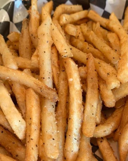 A close-up of golden, crispy French fries sprinkled with black pepper in a checkered paper basket.