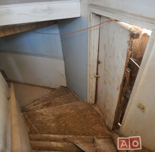 A view of a dimly lit staircase leading to a partially open door with peeling paint and debris on the floor.