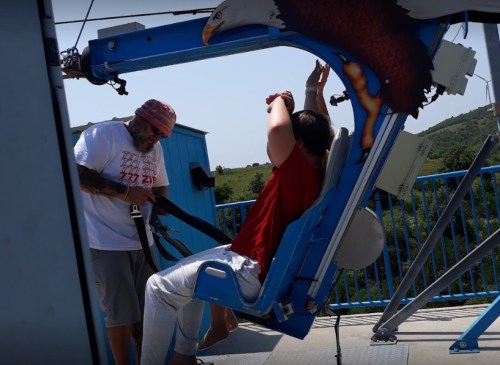 A person in a harness prepares for a ride while an operator secures them, with a scenic background.