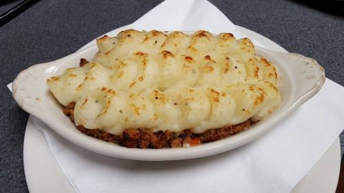 A dish of shepherd's pie with golden-brown mashed potato topping over a savory meat filling, served in a white dish.