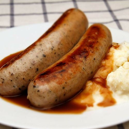 Two grilled sausages on a plate with creamy mashed potatoes and brown gravy.