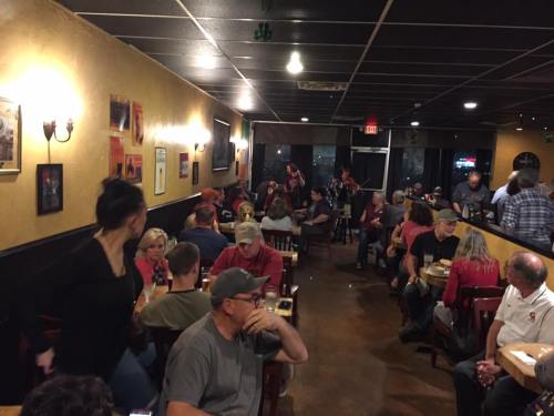 A busy restaurant interior with patrons seated at tables, some enjoying food and drinks, and a lively atmosphere.