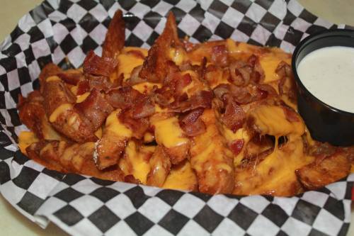 A basket of loaded fries topped with melted cheese, crispy bacon, and a side of ranch dressing.