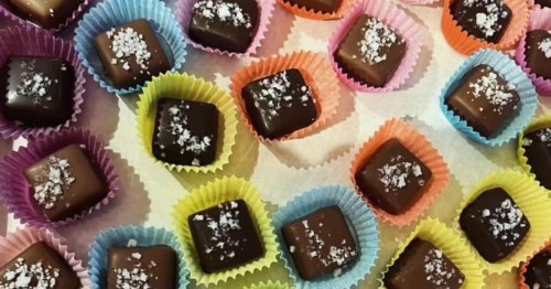 Square chocolate truffles topped with sea salt in colorful, fluted paper liners.