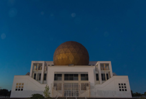 A modern building with a large golden dome against a clear blue sky at dusk.