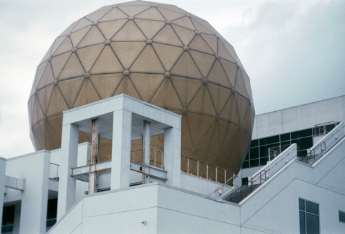 A large geodesic dome atop a modern building, with a staircase leading up to it against a cloudy sky.