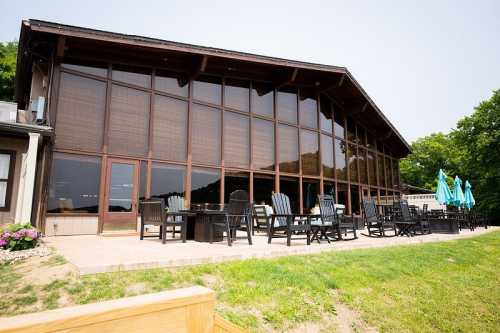 A large wooden building with expansive glass windows, featuring outdoor seating and umbrellas on a grassy area.