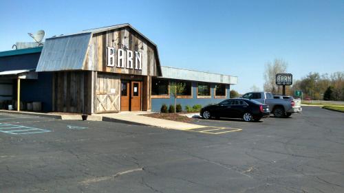 A rustic building with a wooden facade and a sign reading "The Barn," surrounded by a parking lot and clear blue sky.
